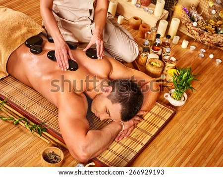 Man getting stone therapy massage in bamboo spa. Lying on floor.