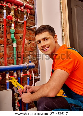 Men builder fixing heating system with special tool. Orange t-shirt.