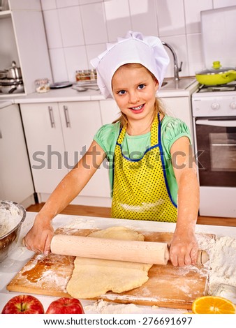 Smiling child female with rolling-pin dough at kitchen.