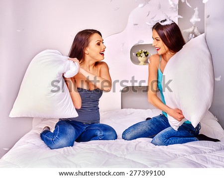 Two lesbian women in jeans at pillow fights in bed.