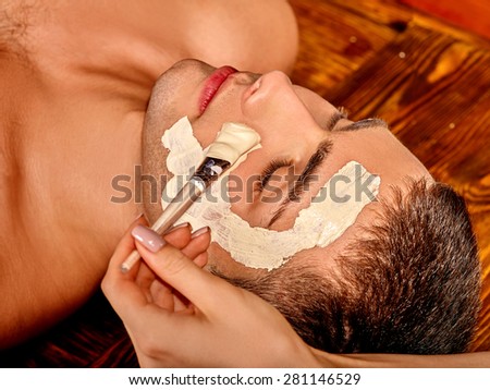 Man getting clay facial mask in beauty spa.