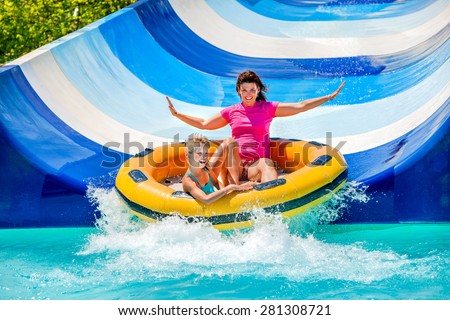 Child with mother on water slide at aquapark. Two persons on summer holiday.