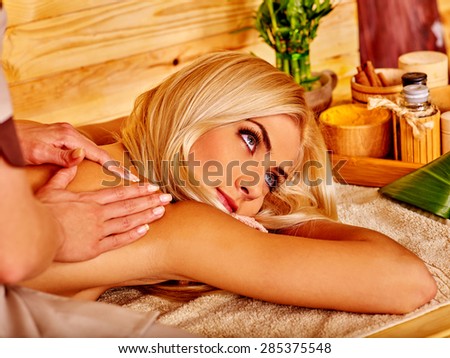 Blond woman getting massage in tropical spa. Not looking at camera.