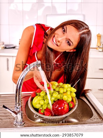 Happy woman washing fruit at kitchen. Pouring water.