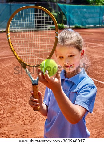 Sport kids girl with racket and ball on  brown tennis court.
