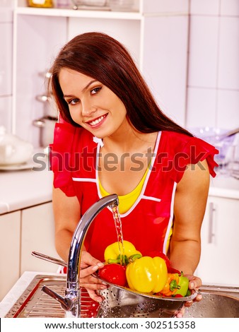 Happy woman washing fruit under water at kitchen.