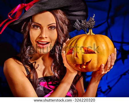 Happy witch holding pumpkin on dark blue background.