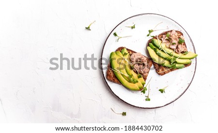 Tuna sandwiches with avocado and microgreen on wholemeal bread, wooden background. Tasty tuna sandwiches for breakfast or snack. Top view, flat lay, copy space.
