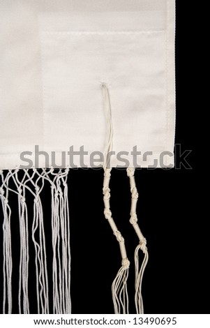 The special fringes, called tzitzit, that are sewn to the edge and corners of a Jewish  prayer shawl, called a tallit, isolated on a black background.