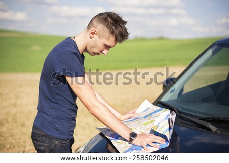 Photo of a traveler parked his car by the side of a  road,  lost and reading the map. Focus on the map and male.