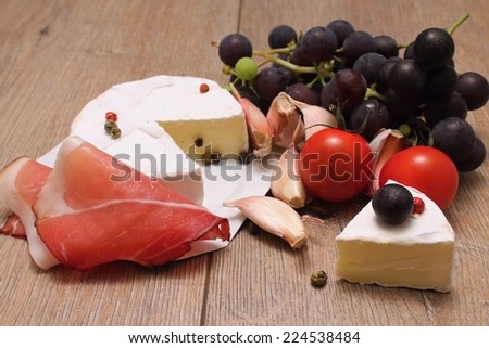 Portion of camembert with ham, wine grapes, tomatoes and garlic and with pieces of color pepper seeds on wooden board