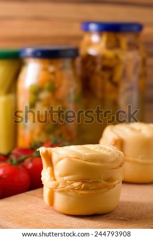 Photo of two pieces smoked cheese parenica on the wooden board with tomatoes and preserved vegetable and mushrooms in background.