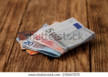 Horizontal photo with three euro bills folded in the middle and two credit cards under them placed on old worn wooden board.