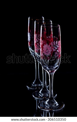 Vertical photo of three glasses placed on black background. Glasses are in a row with small overlapping. Glasses are for vine and have red flower ornament on.
