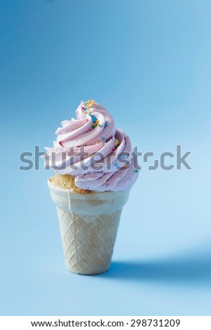 Cupcake in an ice-cream cone - perfect summer dessert for an outdoor birthday party. Strawberry buttercream icing contrasting with sky blue background.