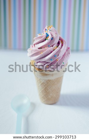 Cupcake in an ice-cream cone - perfect summer dessert for an outdoor birthday party. Strawberry buttercream icing and sprinkles match striped background.