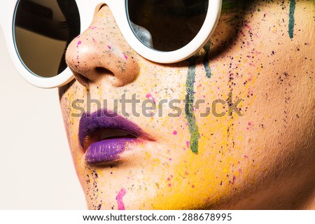 Portrait of model wearing sunglasses. Close-up portrait of young woman with unusual makeup. Model posing with paint drops over her face. Creative makeup.
