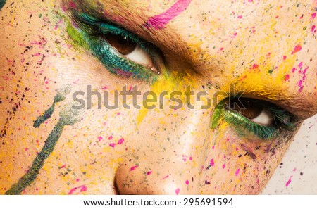 Close-up portrait of young woman with unusual makeup. Model posing with paint drops over her face. Creative makeup.