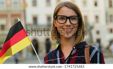 Caucasian woman in casual shirt with german flag posing on camera and smiling on the city street background. 商業照片 © 