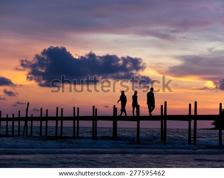 Silhouette figure of people walking relax on a big teakwood bridge during sunset (on sea pier)