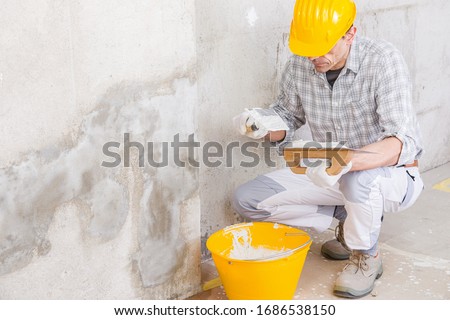 Plasterer covering a stained damp patch in a white wall with new plaster or masonry during renovations or maintenance on a house interior ストックフォト © 