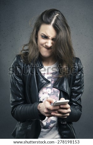 Closeup portrait angry young girl looking at phone seeing bad news or photos with disgusting emotion on her face texture background. Human emotion, reaction, expression