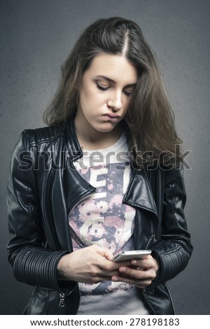 Closeup portrait tired young girl looking at phone seeing bad news or photos with bored emotion on her face texture background. Human emotion, reaction, expression