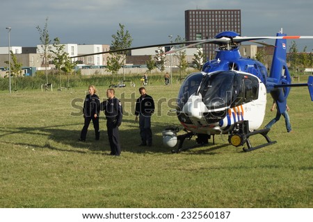 ALMERE,  THE NETHERLANDS - SEPTEMBER 2, 2013: Dutch police helicopter stands on grass in a urban park with police investigators and a pilote standing beside the law enforcement aircraft.