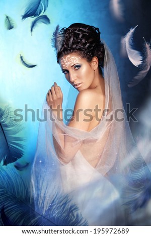 Beauty Woman. Holiday Make-up. Queen High Fashion Portrait over Blue with Feathers Background. Eye shadows and Crystals on ? forehead and Body-art, Pattern. Princess Swan with Fashion Hairstyle.