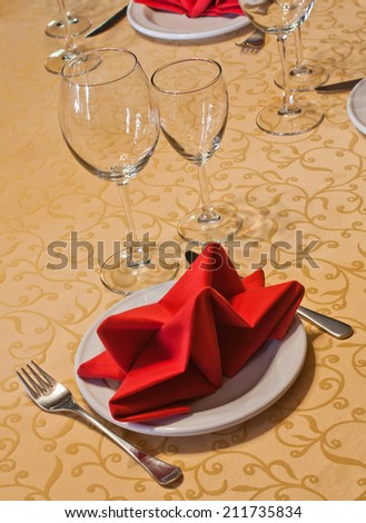 Hotel service: table in a restaurant with a white tablecloth, red napkins, wine glasses and cutlery.