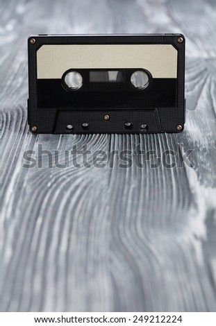 Music concept. Black audio cassette on the gray wooden background. Vintage, retro style. Soft focus.