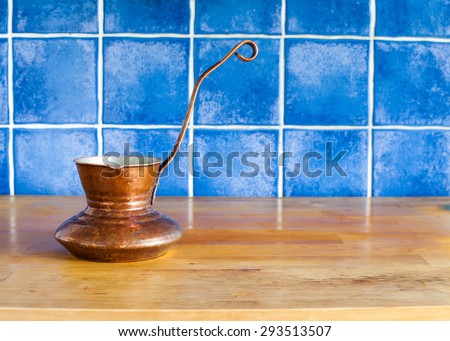 Vintage copper coffee maker, turk on the kitchen table. Blue tile wall. Copy space. Soft focus.