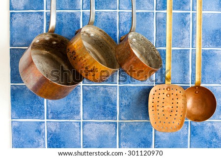 Kitchen interior and cookware. Hanging retro design copper kitchenware set. Pot, spoon, skimmer, colander. Blue tiles ceramic background, aged sand wall texture. copy space.