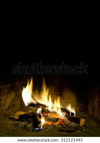 Christmas vacation postcard template. Chimney place against dark background. Flames of fire in a fireplace. Realistic fire. Copy space, black background.