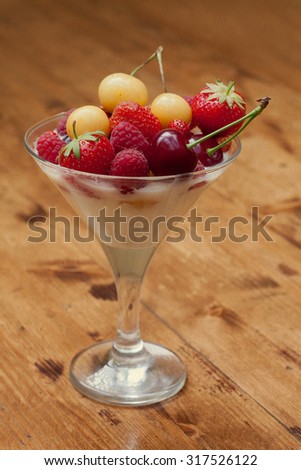 Creamy dessert with fresh summer fruits in cocktail glass. Yellow and red cherry, strawberry on top. Wooden background. soft focus. toned vintage paper texture!