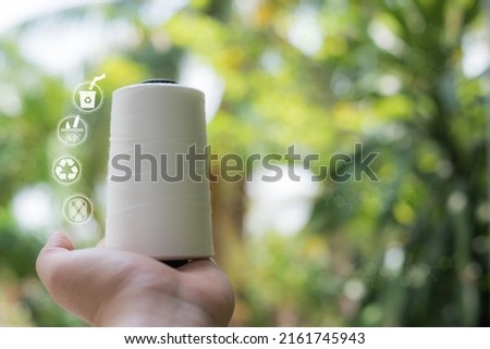 Hand holding Raw White Polyester FDY Yarn spool, Polyester Filament Yarn spool.PET fiber Yarn,spun polyester sewing thread with blurred green background. Recycle icon, sustainable icon and Bottle icon Foto stock © 