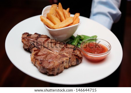 Waiter offering T-bone steak with french fries and hot sauce