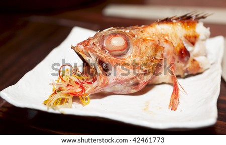 Half-eaten bbq fish with salad in its mouth
