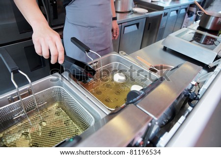 Chef cooking dish in a deep fryer in boiling oil on restaurant kitchen