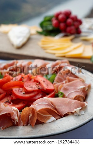 Platter with cured ham on table, radish and cheese in the background