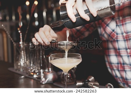 Bartender is straining drink in a glass, toned, misty, bleached colors