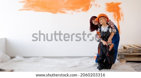 Home repairs. Happy family mom and son painted the wall orange. Wall painting. Renovation or remodel room concept. Woman and child in helmet on wall background. Banner. Place for text. Foto stock © 