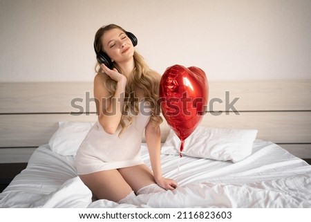 Valentine's Day, Women's Day, Anniversary or Anniversary. a woman in a headphone sits in bed and celebrates February 14 with a red heart-shaped foil balloon. listen to music and relax. banner Stock fotó © 