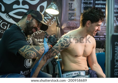 ROME - MAY 11: Tattoo artist draws with his tattoo machine on client\'s arm a tribal design in his workshop on May 11, 2014 in Rome.