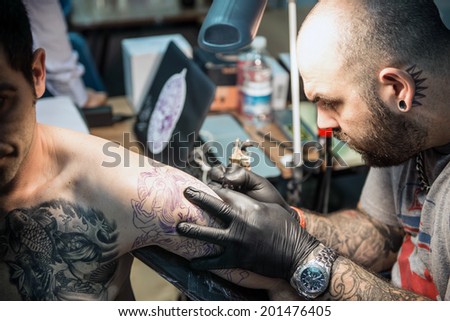 ROME - MAY 11: Tattoo artist draws with his tattoo machine on client\'s arm a tribal design in his workshop on May 11, 2014 in Rome