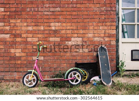 Old skateboard and push scooter over a brick wall