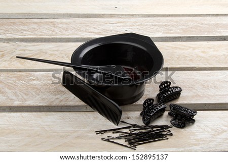 Hair color brush, and bowl with comb, hair clips and pins on wooden surface
