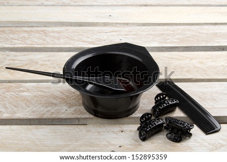 Hair color brush, and bowl with comb and hair clips on wooden surface