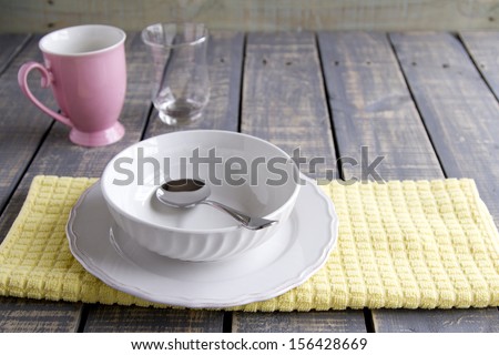 Bowl, plate and spoon on a cloth with glass and mug on wood table
