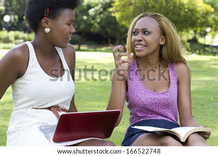 Beautiful black woman on grass with a book and a laptop
